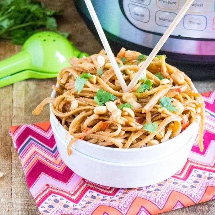 peanut chicken pasta in a white bowl with chopsticks in it 