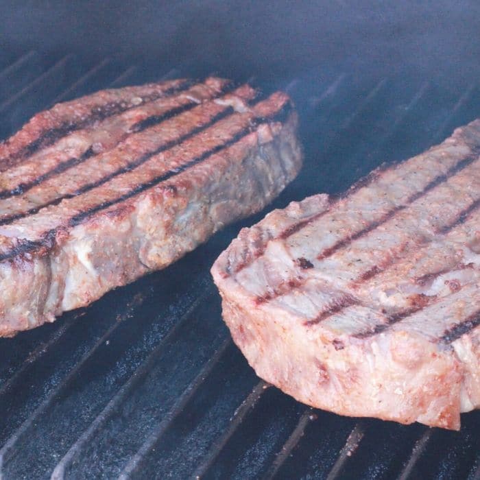 longhorn steak seasoning rubbed on large steaks on grill with man grates 