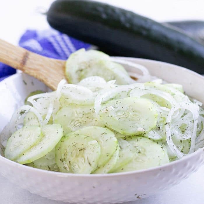 cucumber onion salad in white bowl with wooden spoon