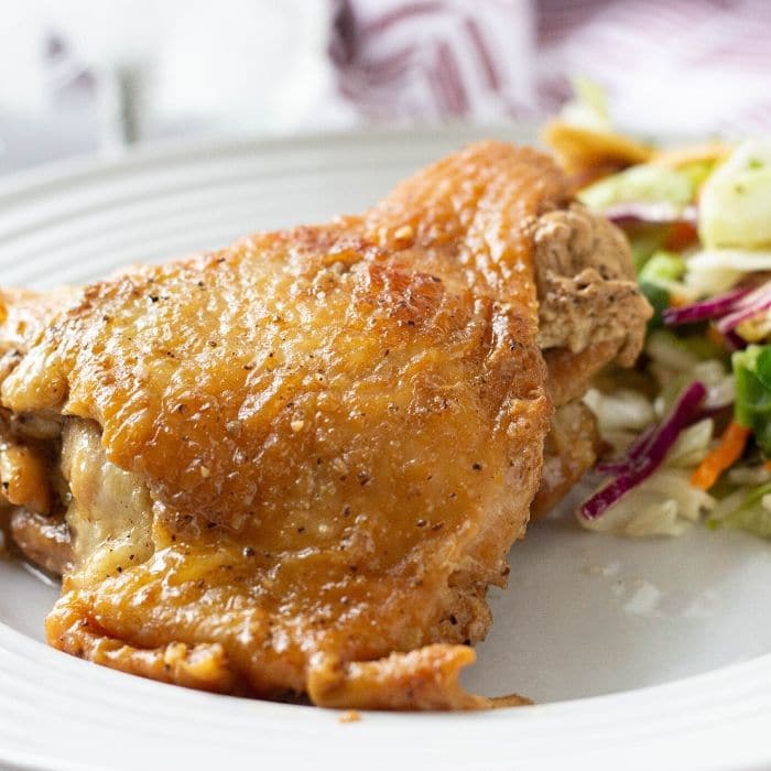 honey garlic chicken thigh on plate with salad by it 