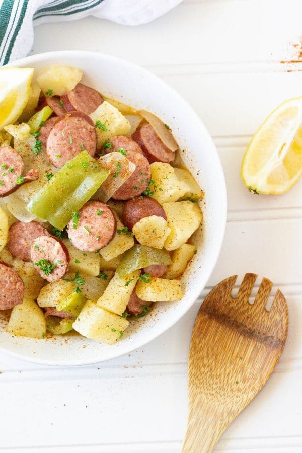 sausage and potatoes in a bowl with spoon and lemon by it