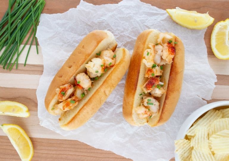 lobster rolls with lemons and chips beside it