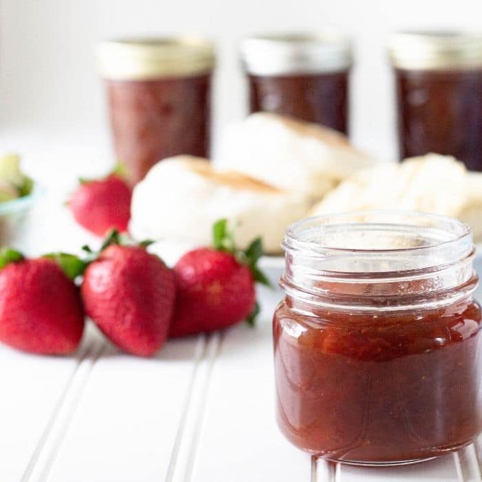 jar of strawberry rhubarb jam on table with fresh strawberries in background 