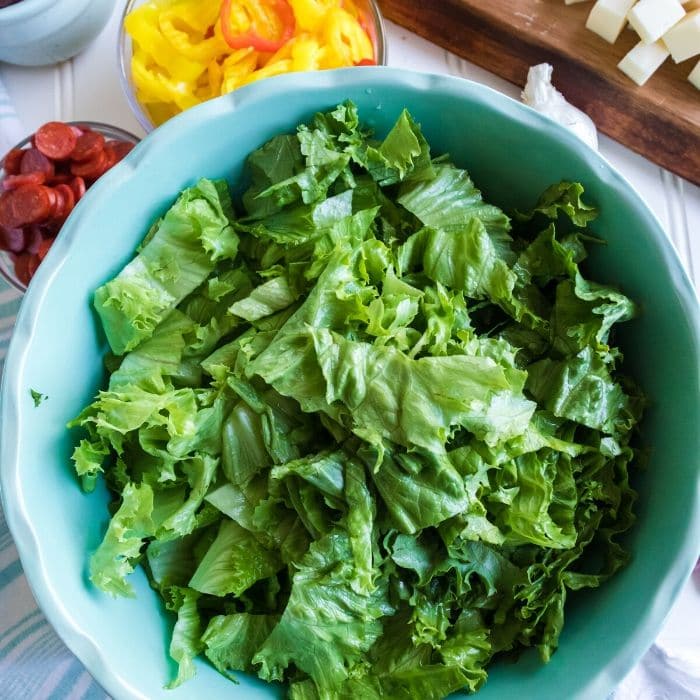 bowl of lettuce with other salad ingredients around it 