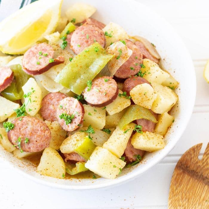 smoked sausage and potatoes in a white bowl with spoon by it