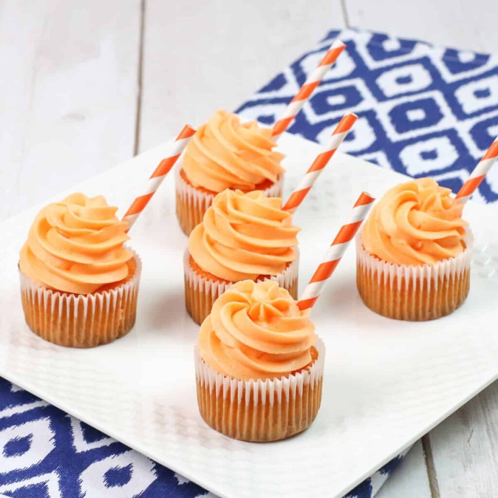 plate with orange cream soda cupcakes with a paper straw sticking out on side of frosting 