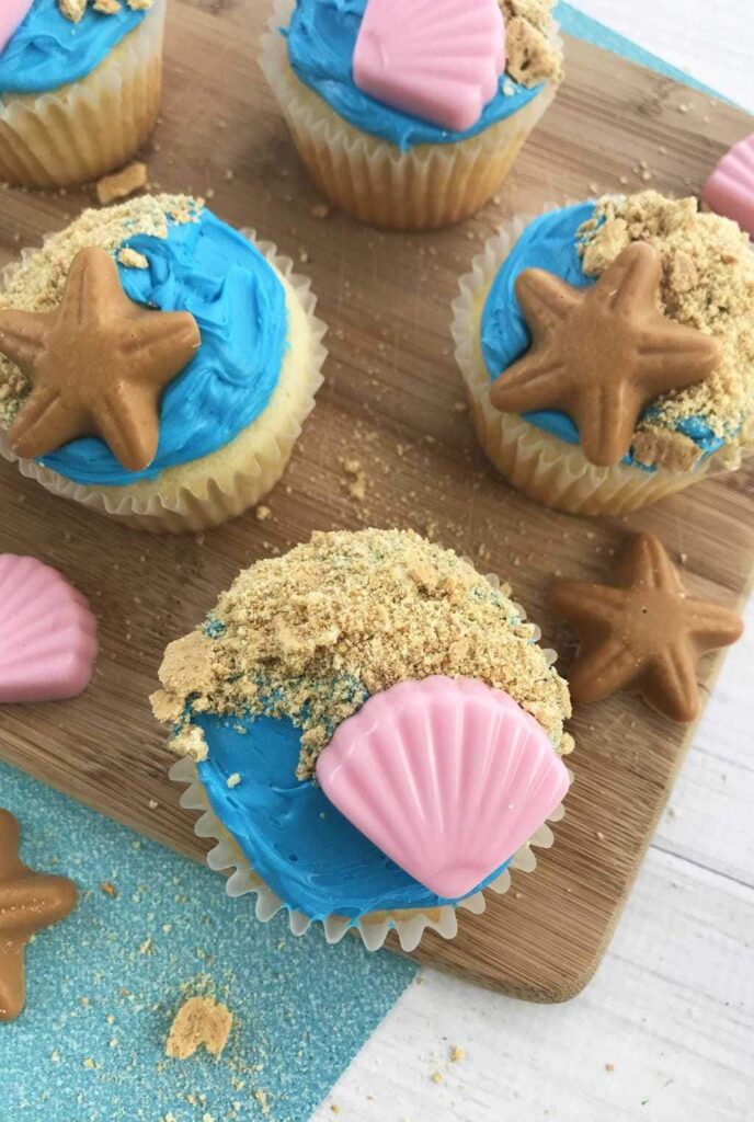 seashell topped beach style cupcakes on a wooden table 