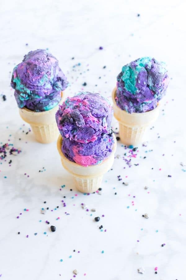 galaxy ice cream in ice cream cones on white table with sprinkles around it 