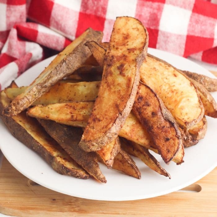 potato wedges piled on a plate with red checkered napkin behind it 