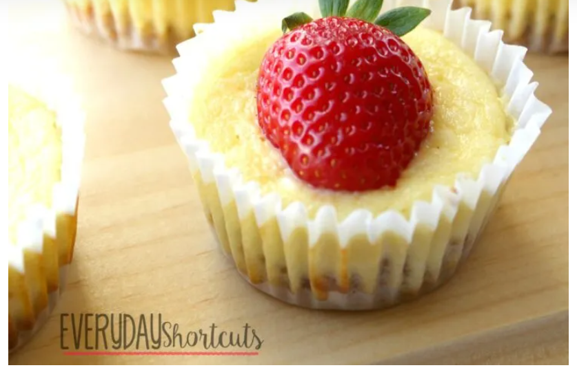 side view of a cheesecake cupcake with a strawberry sitting on top on a wooden table