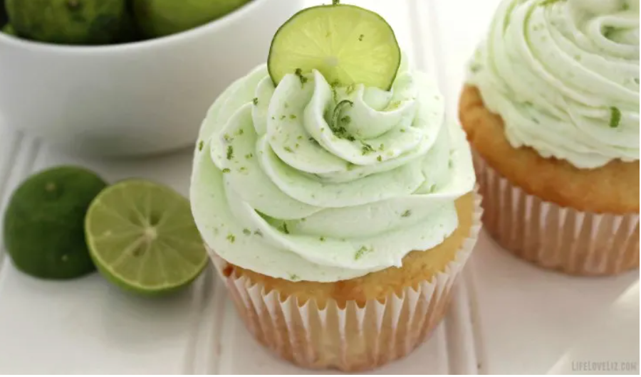 key lime cupcakes sitting on wooden table with key limes sliced in half sitting by the cupcakes