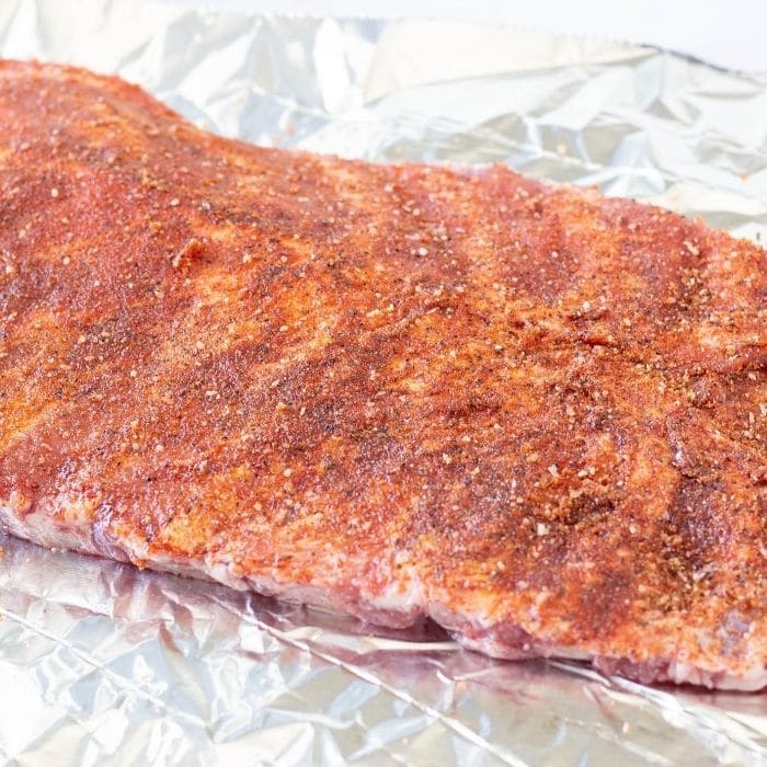 bbq ribs with a dry rub smeared on sitting on aluminum foil