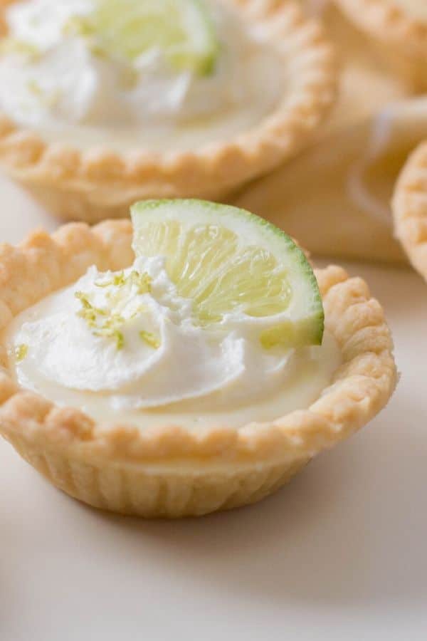 mini lime pie on table topped with whip cream, lime zest and a lime wedge. 