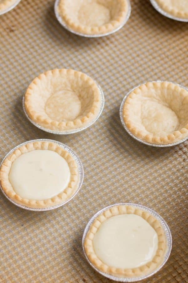 mini lime tartlets on a baking sheet with some tarts filled with key lime filling others are empty. 