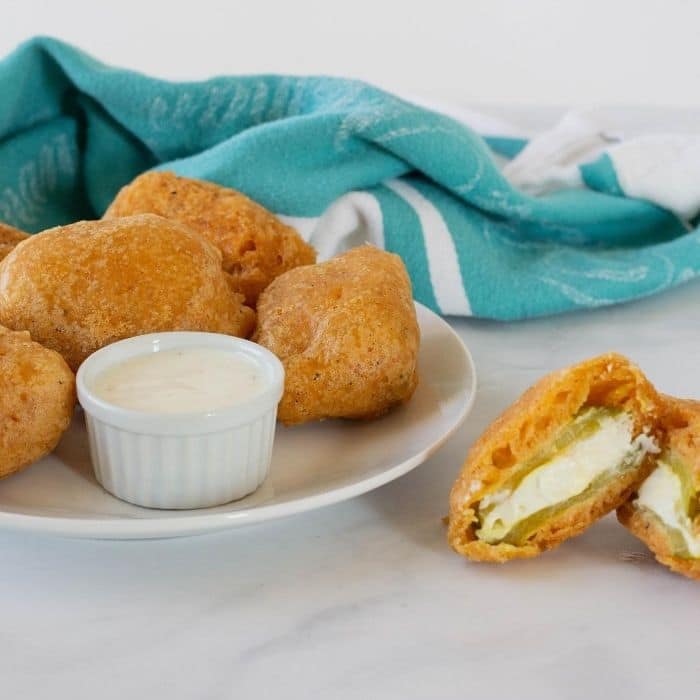 fried picles on a plate with one cut open to see it is stuffed with cream cheese 