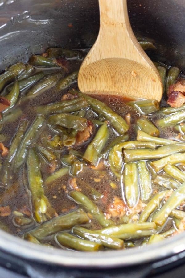 instant pot with green beans and bacon along with wooden spoon