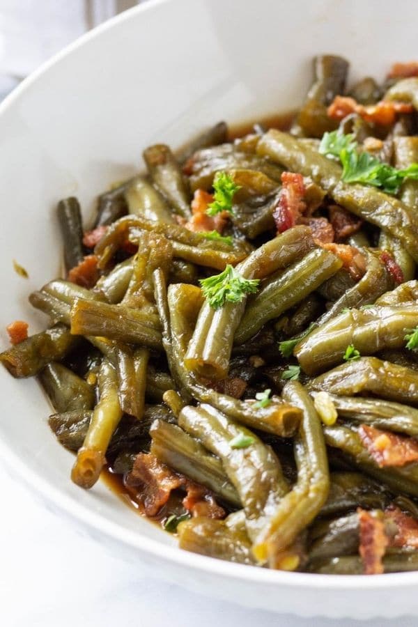 white bowl of green beans and bacon topped with parsley 