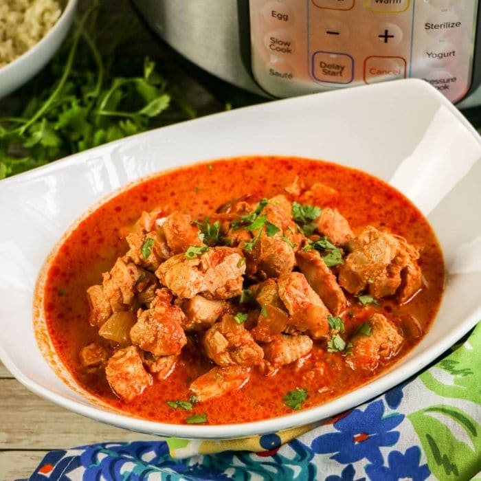 white bowl of chicken topped with cilantro and instant pot behind it