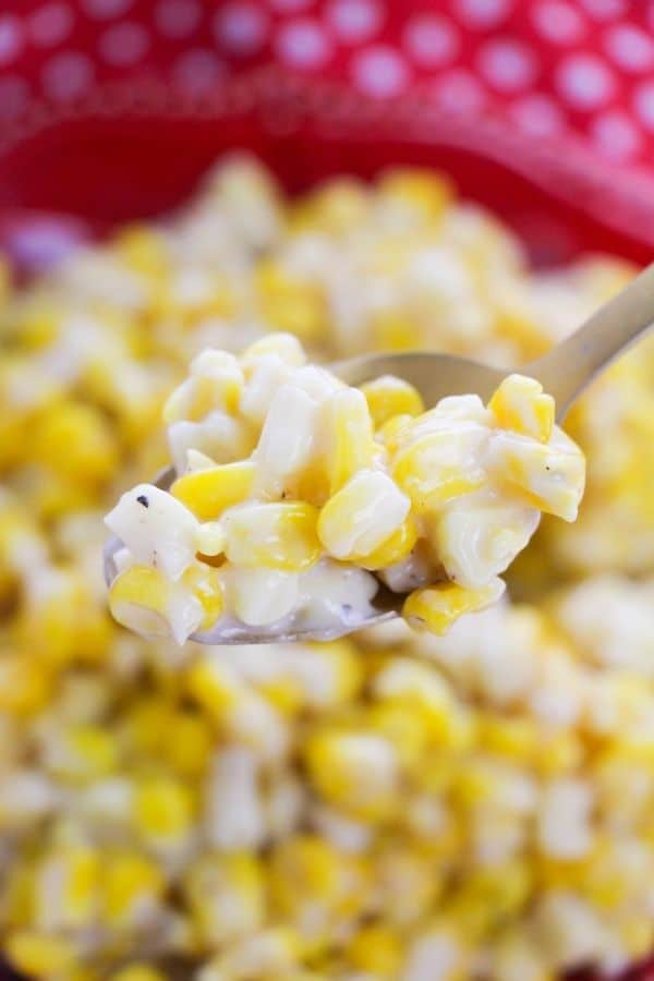 spoon of corn with plate of corn under it 