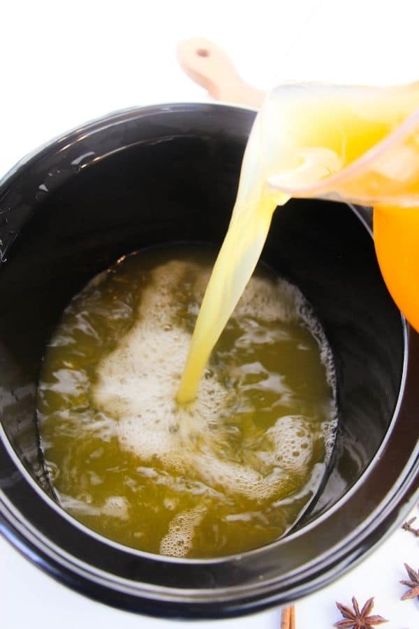 apple cider pouring into crockpot