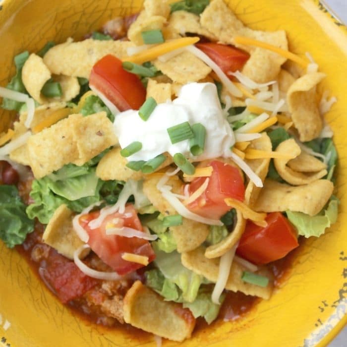 chili pie in a yellow bowl topped with cheese, sour cream, and other taco toppings