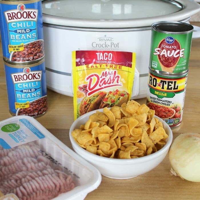 ingredients for frito pie on table with crockpot behind it 