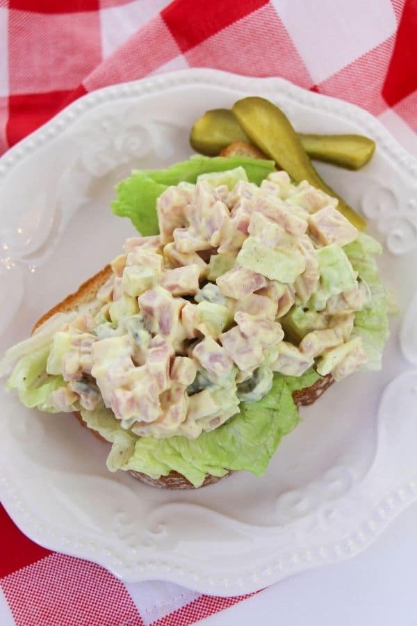 ham salad sandwich on a plate with pickles by it 