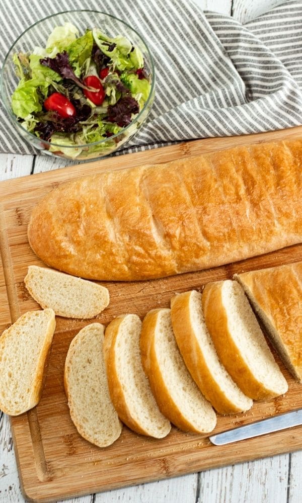 artisan bread on cutting board with salad behind it 