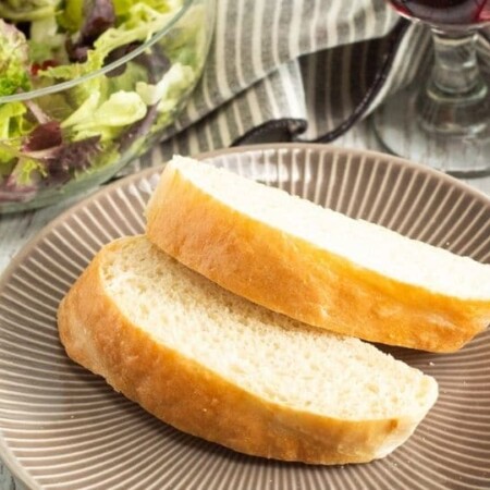 french bread on a plate with salad and wine behind it on table