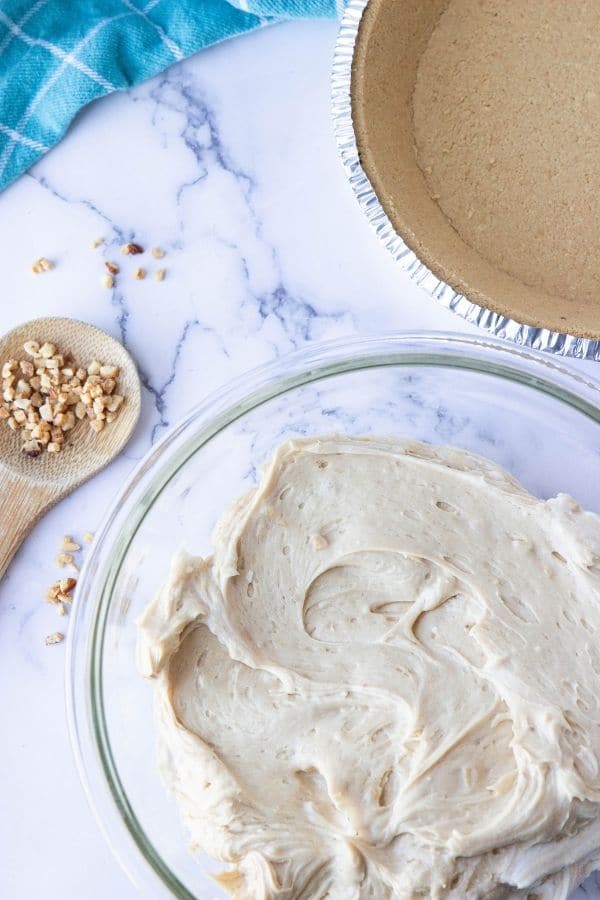 peanut butter pie filling in bowl, graham cracker crust by it, and spoon with nuts 