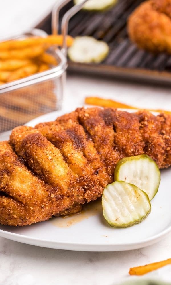 nashville seasoned chicken on white plate with fries and chicken behind it on table