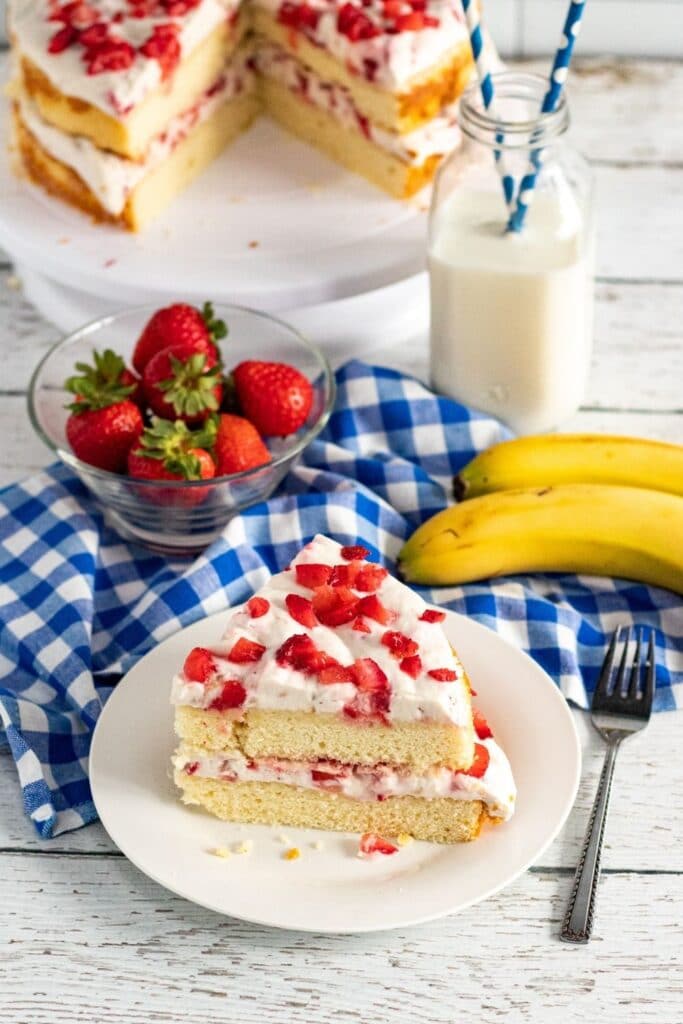 slice of strawberry cake on plate with layered cake behind it 