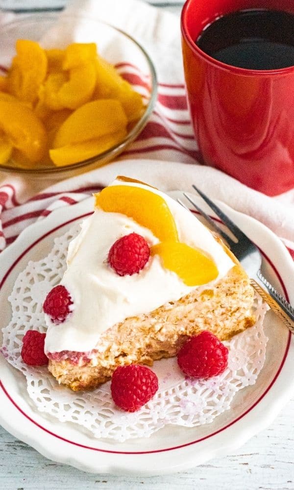 slice of cheesecake on plate with peaches and coffee behind it 