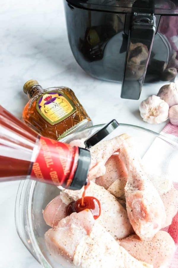 barbecue sauce being poured over raw chicken in a bowl 