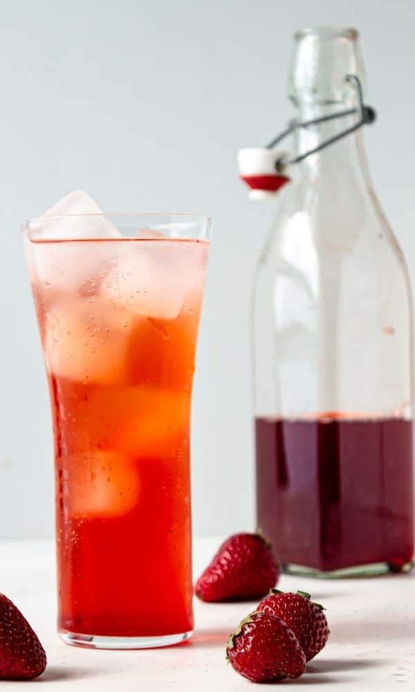 flavored syrup in jar and drink with berries around it on table