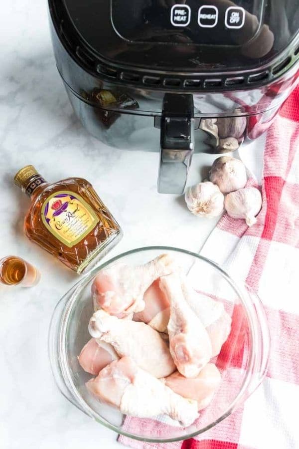 chicken legs in a bowl with whiskey and air fryer beside it 