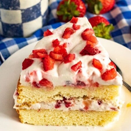 slice of strawberry cake on a plate with blue checkered towel behind it