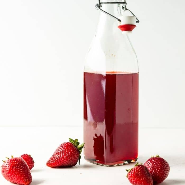 glass jar of fruit syrup on counter with berries in front 