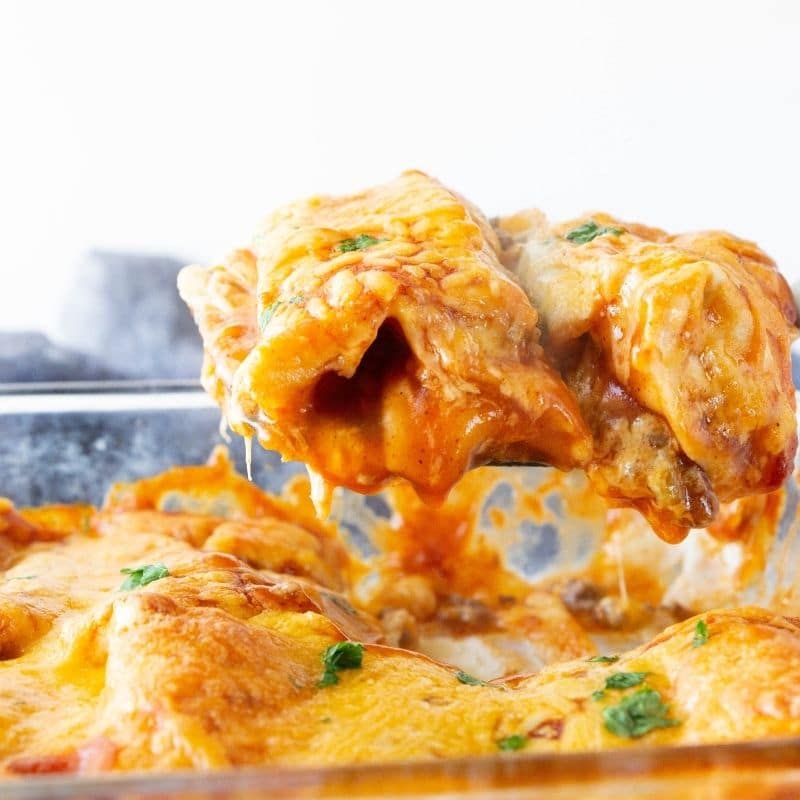 cheesy enchiladas lifting out of pan