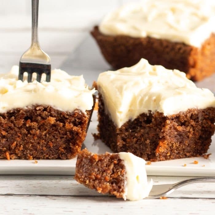 fork poked in carrot cake with bite taken out of another carrot cake slice 