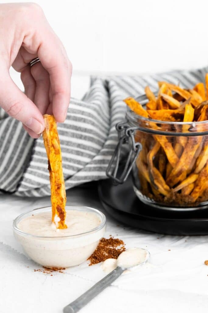 dipping sweet potato fry in homemade sauce on counter 