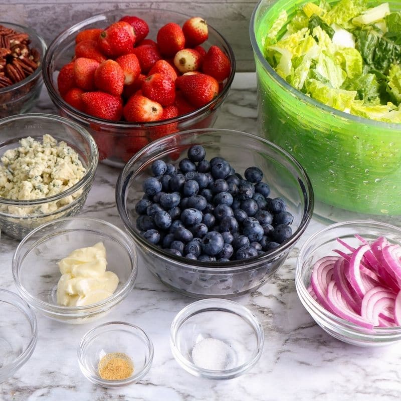 green salad ingredients on counter all in different bowls 