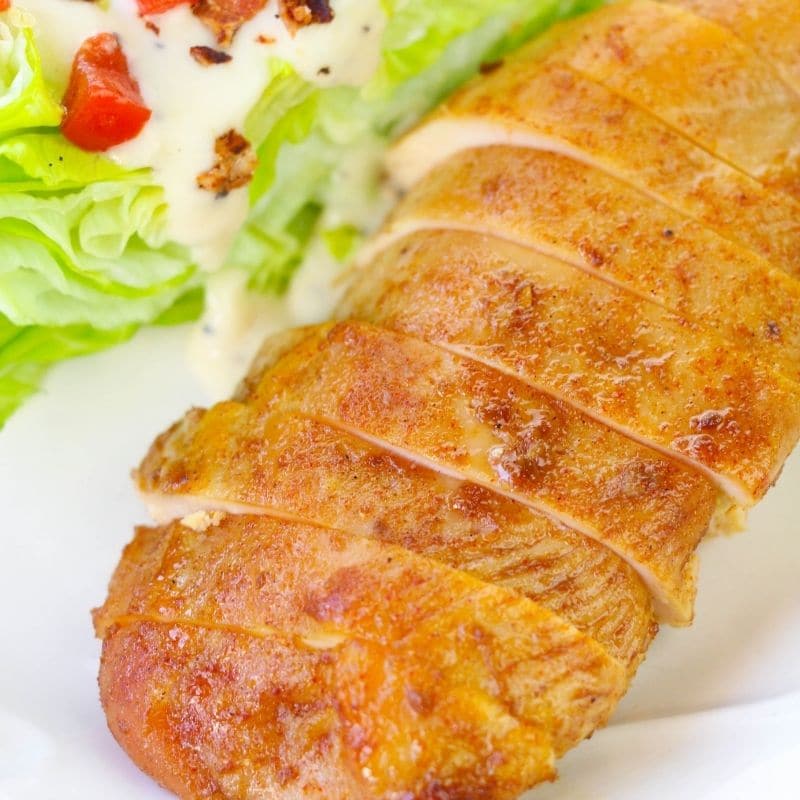 sliced chicken on a plate with salad behind it 