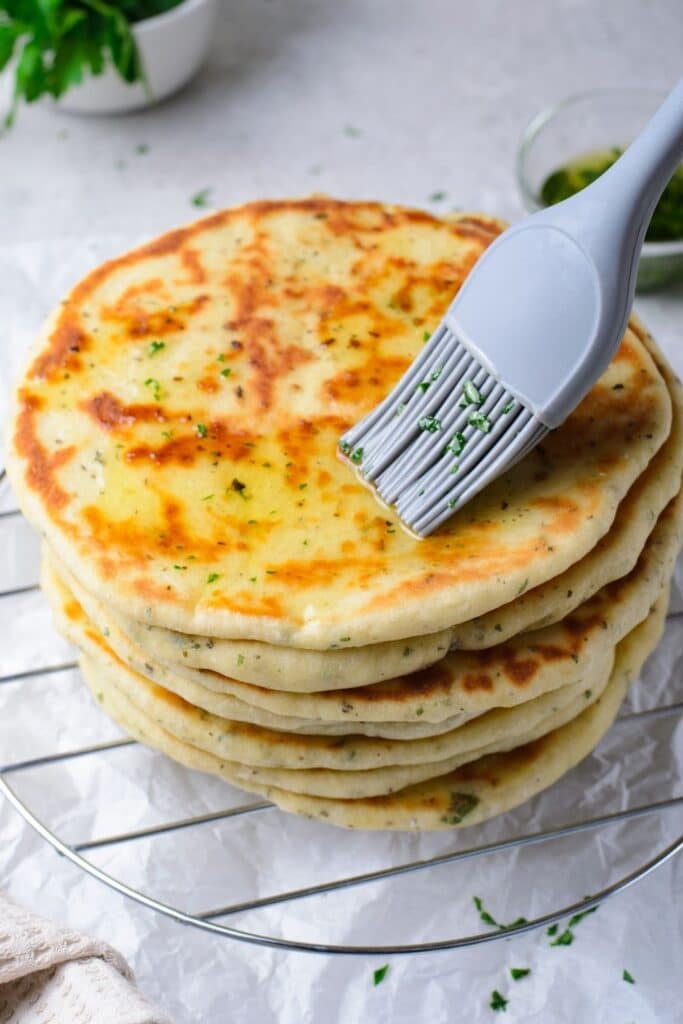 brushing oil on naan flatbread on cooling rack