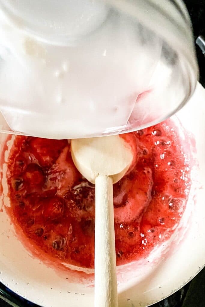 strawberry glaze in a pan getting thickened up with cornstarch slurry