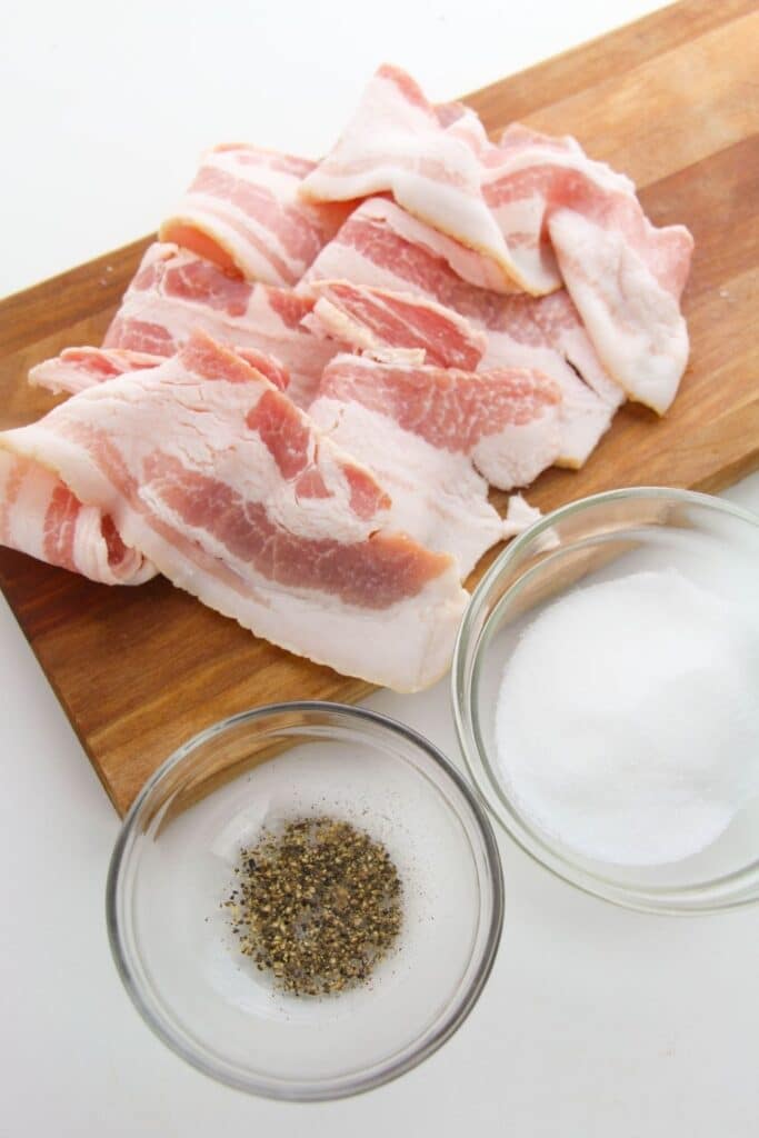 raw bacon on cutting board with pepper and sugar beside it in bowls 