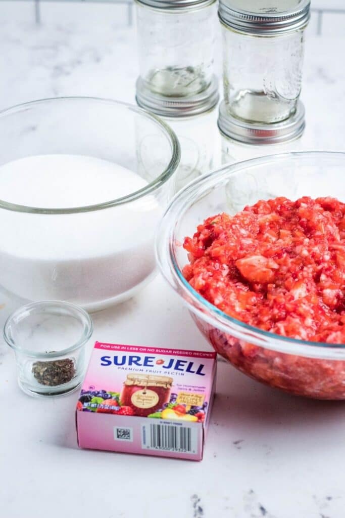 ingredients for jam on counter - strawberries, sugar, pectin, mint 