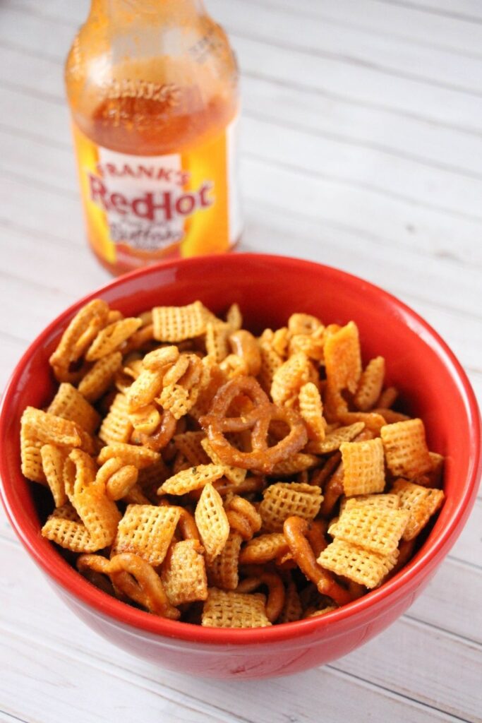 chex mix on table with hot sauce behind it 