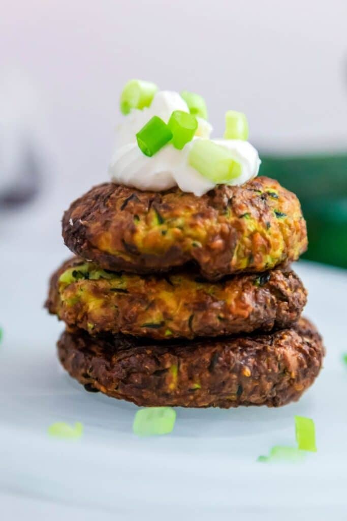 stacked fritters on plate with green onions on top 
