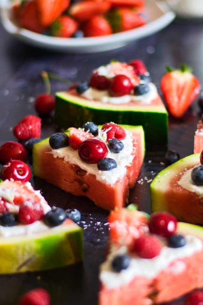 fruit pizza on black counter with berries around it 